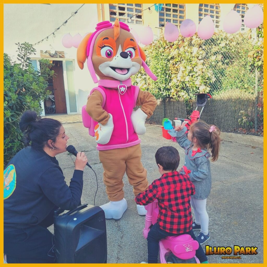 Dos niños junto a una monitora con micrófono y una persona disfrazada de Skye de La Patrulla Canina